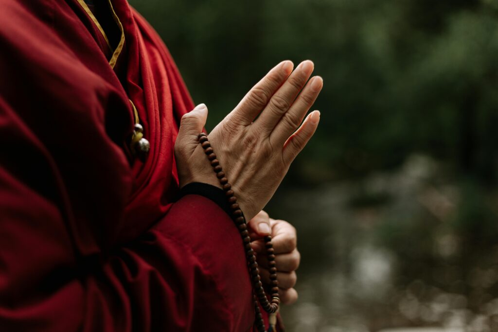 Close-up of monk in red robe meditating with prayer beads outdoors.