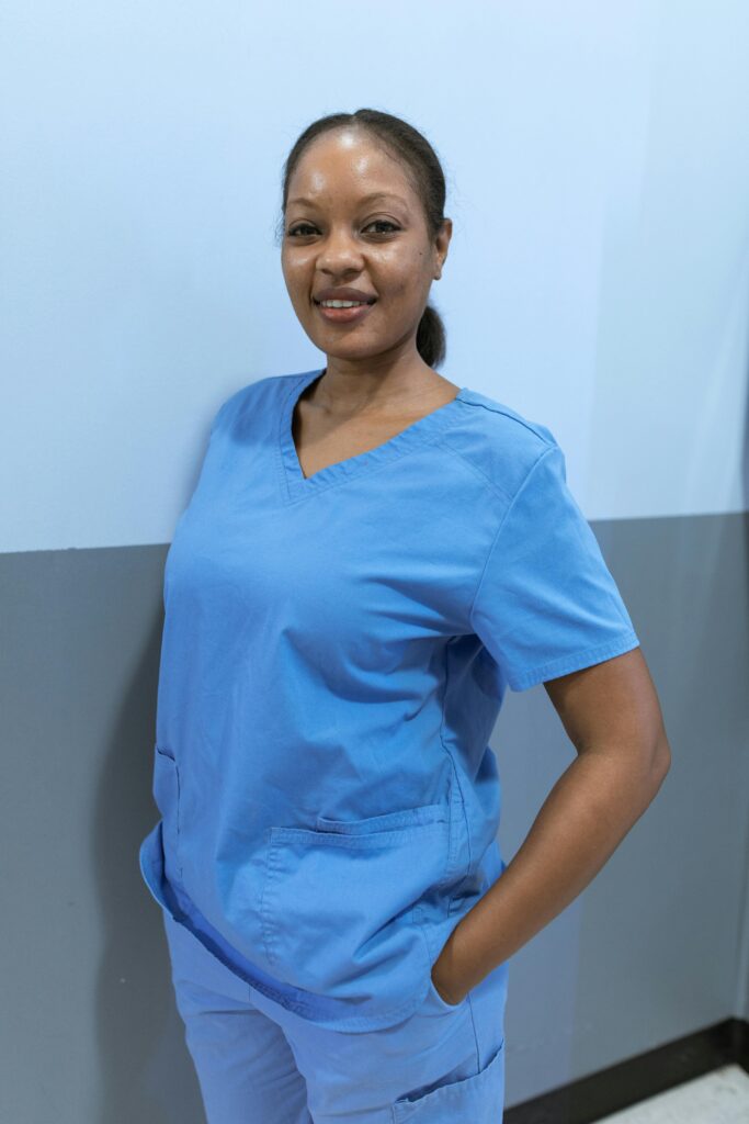 African American nurse smiling confidently indoors, wearing blue scrubs.