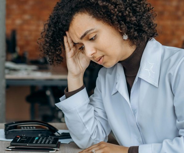 Exhausted woman in office with paperwork, displaying signs of stress.